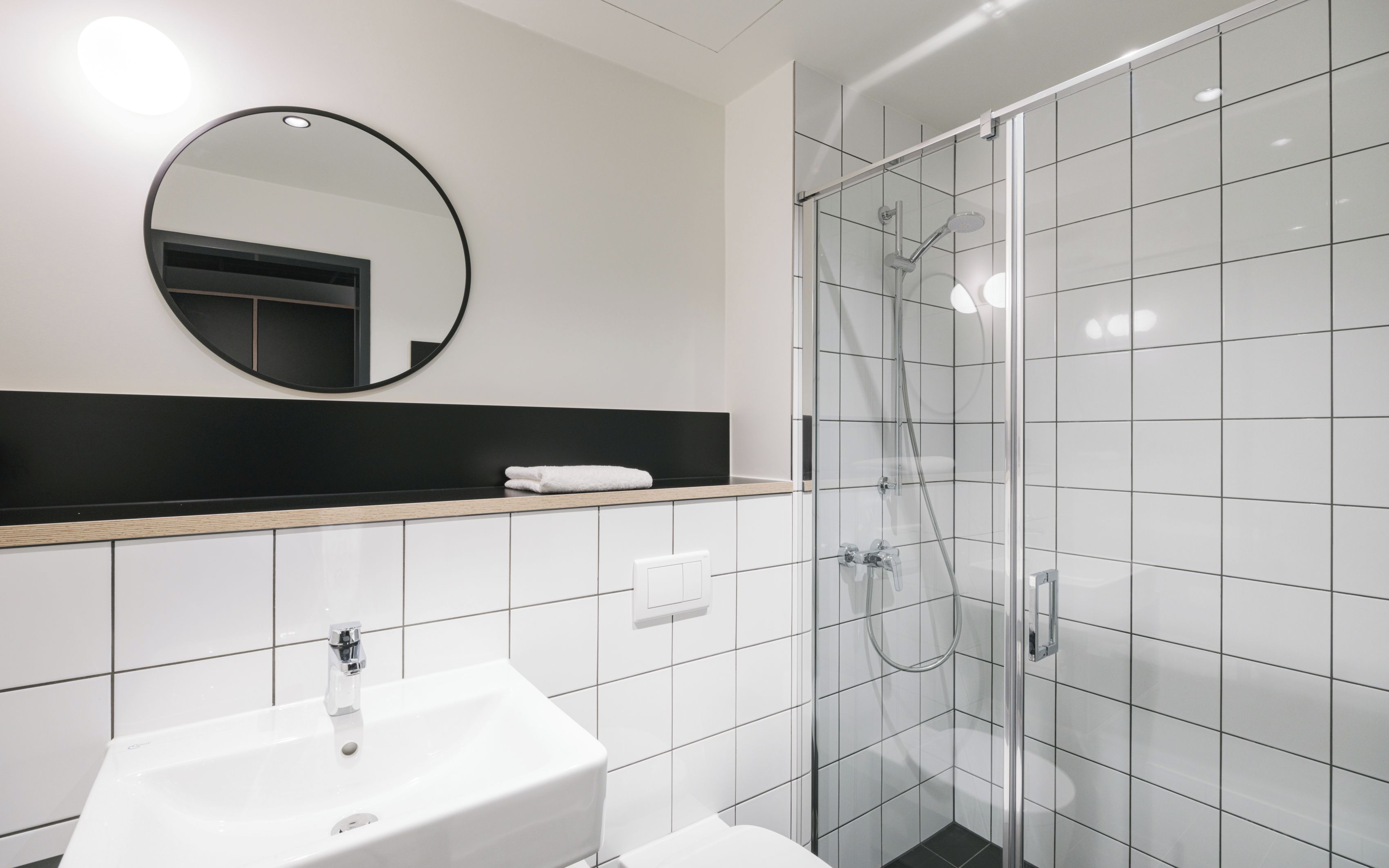 Une salle de bain moderne avec un lavabo blanc, un miroir et une douche à parois de verre.