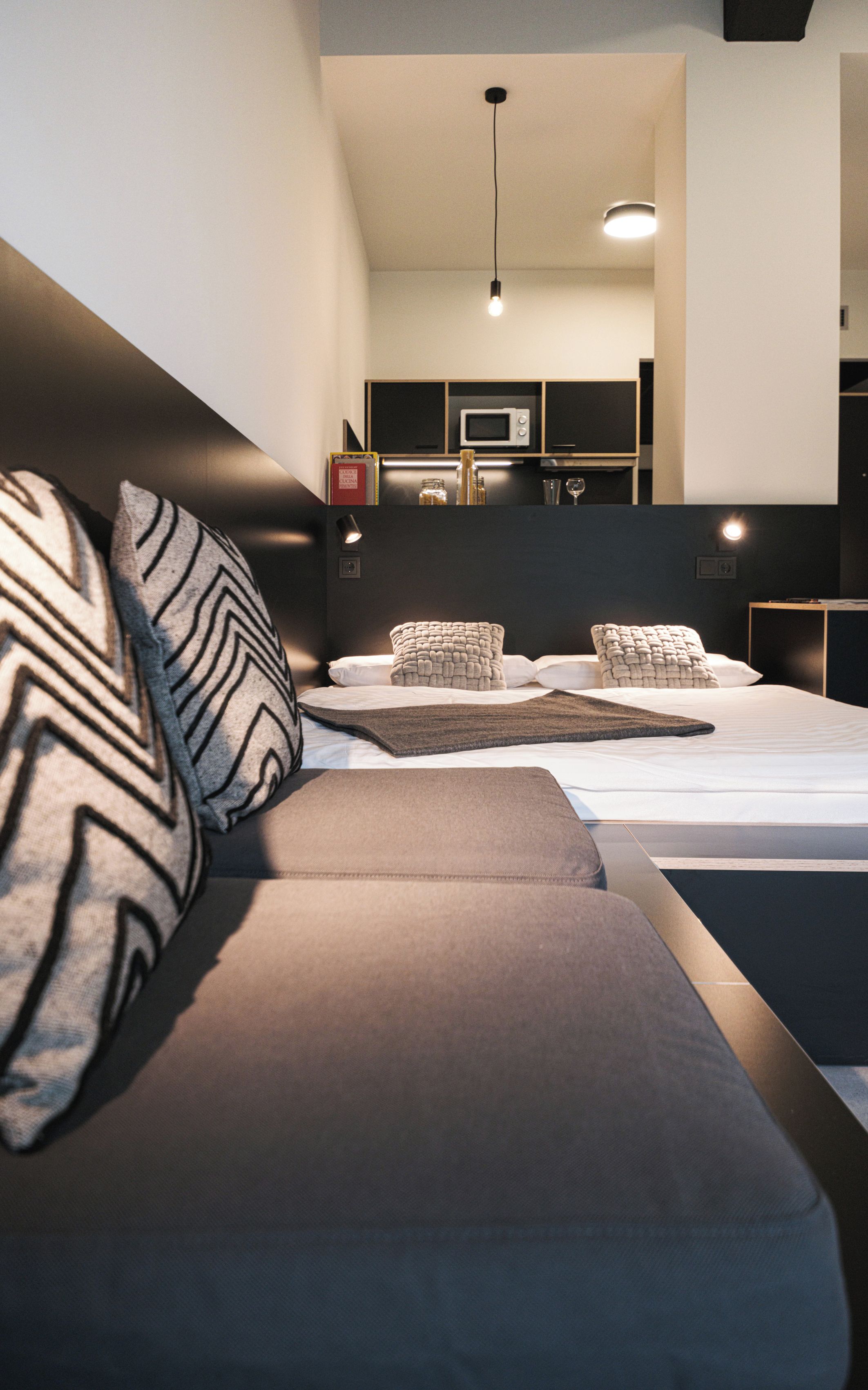 Quarto moderno com sofá-cama, mesa de cabeceira e estante embutida para televisão.