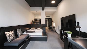 Une chambre d’hôtel moderne équipée d’un canapé, d’un lit, d’un bureau, d’une télévision et d’une kitchenette.
