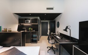 A modern bedroom with a bed, a desk with a computer, and a kitchenette area. - Moliving - Design Hotels & Apartments - Free Gym (Neuss)
