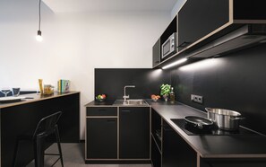 A modern kitchen with black cabinetry, a stainless steel sink, and a black countertop. - Moliving - Design Hotels & Apartments - Free Gym (Neuss)