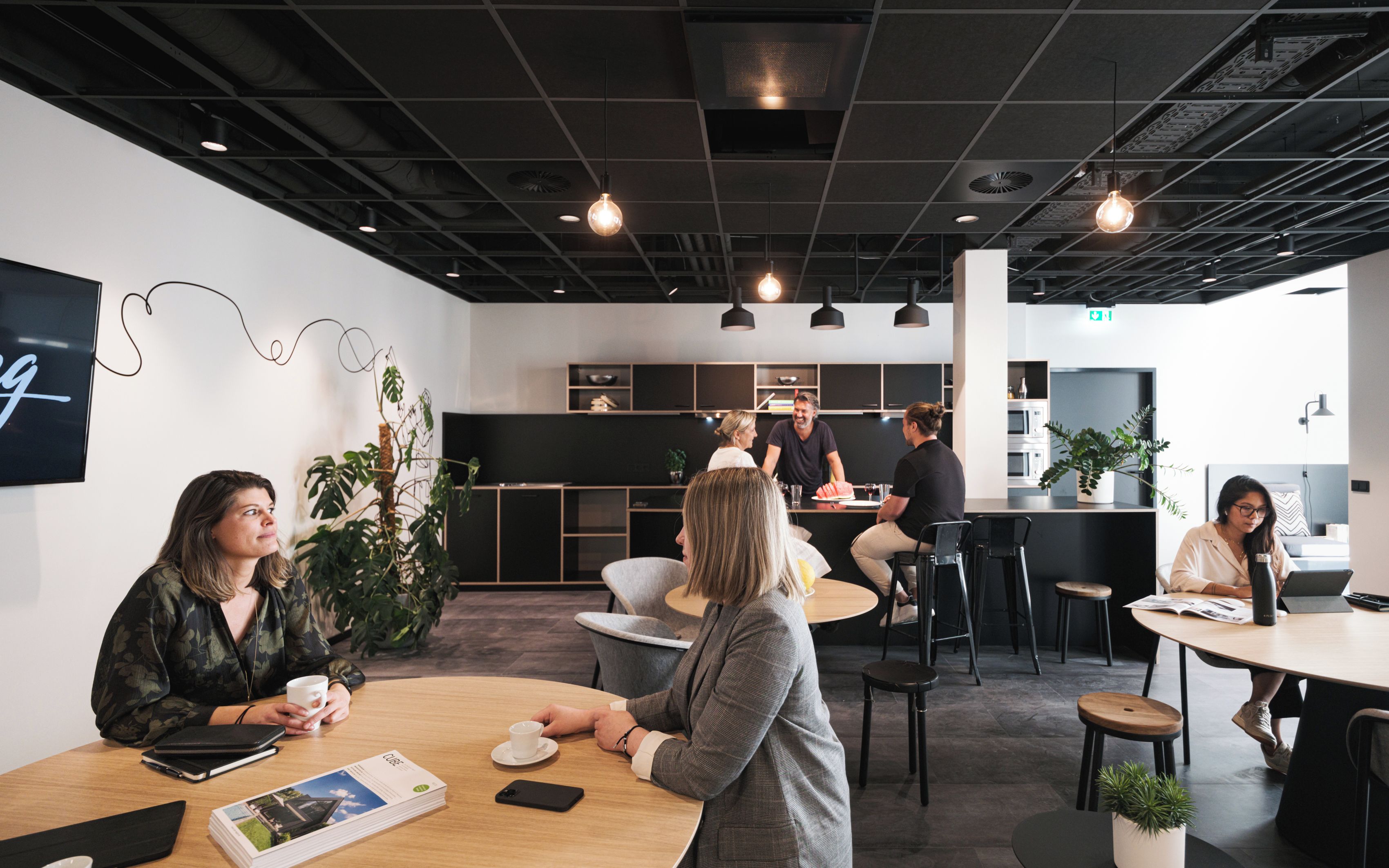A modern office space with round tables, black chairs, and pendant lighting.