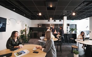 Un espace de bureau moderne avec des tables rondes, des chaises noires et des luminaires suspendus.