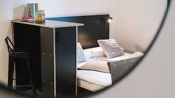 Quarto compacto com uma cama, uma escrivaninha e uma cadeira.