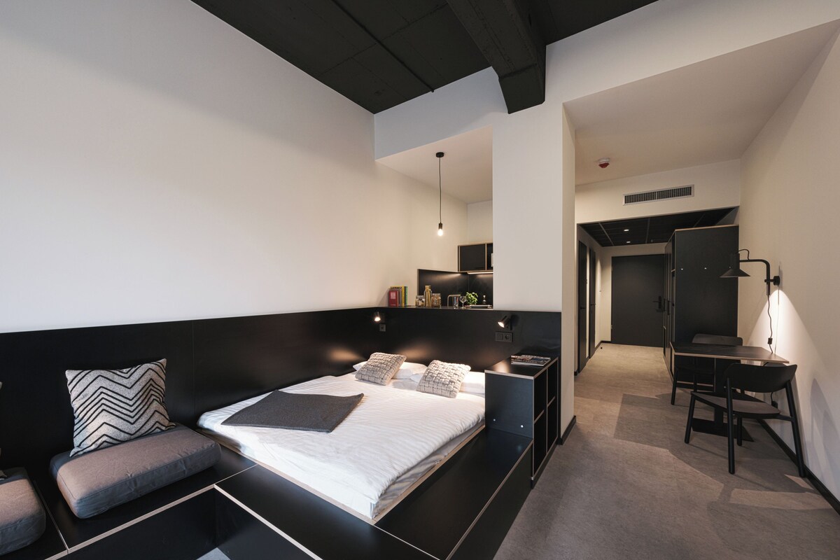 A modern bedroom with a large bed, a desk, and a seating area.