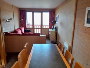 A room with a wooden table and chairs, a sofa with red cushions, a desk with a computer, and a window with curtains. - 200m from ski slopes, 1st floor, view valley, balcony, tv, ski locker, 45m², Montchavin La Plagne (Bellentre)