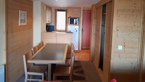 Ett kompakt kök med träskåp, ett matbord med stolar och ett litet kylskåp.