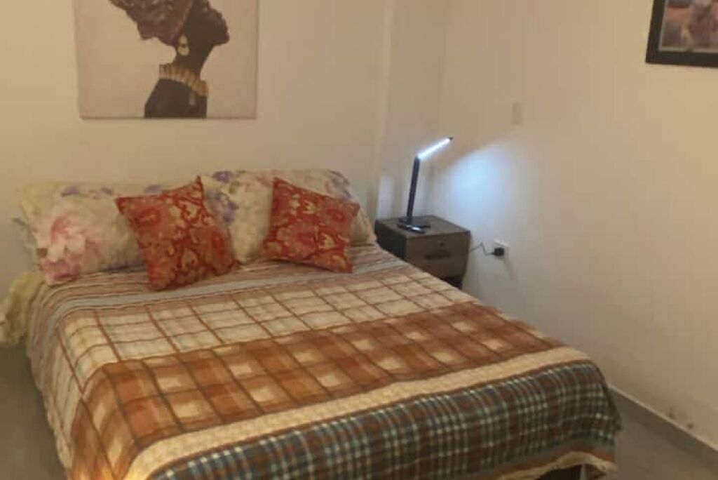 A bedroom with a bed, pillows, a nightstand, and a wall-mounted lamp.