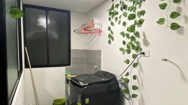 Une buanderie équipée d’un lave-linge, d’une serpillière, d’un seau et d’un panier de basket fixé au mur.
