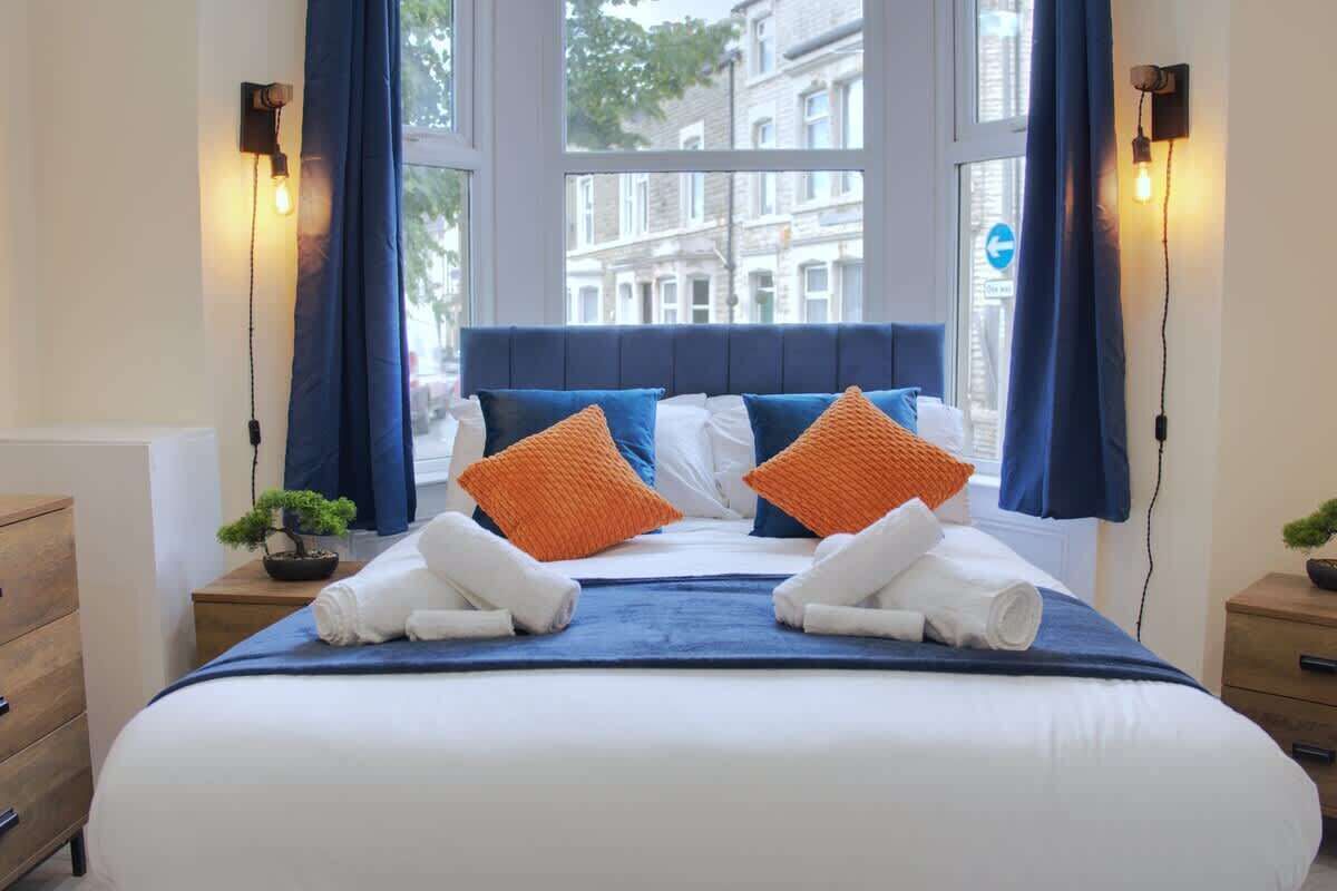 Une chambre d’hôtel avec un grand lit, deux tables de chevet, une commode et une fenêtre avec des rideaux.