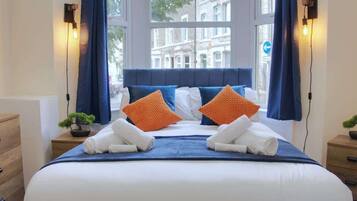 Une chambre d’hôtel avec un grand lit, deux tables de chevet, une commode et une fenêtre avec des rideaux.