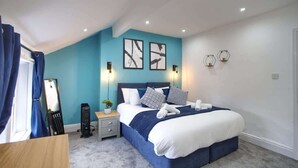 Um quarto com cama, mesas de cabeceira, espelho e quadros nas paredes.