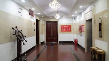 A hotel corridor with a chandelier, a ship's wheel, and a red sign on the wall.