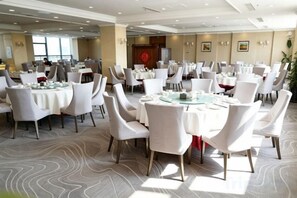 A banquet hall with round tables, white chairs, and a patterned carpet.