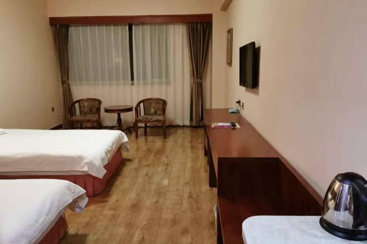Une chambre d’hôtel avec deux lits, un bureau, une chaise, une télévision et une bouilloire.
