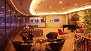A modern lounge area with seating, a piano, and a digital screen. - Shenyang Airport Hotel (SHENYANG)