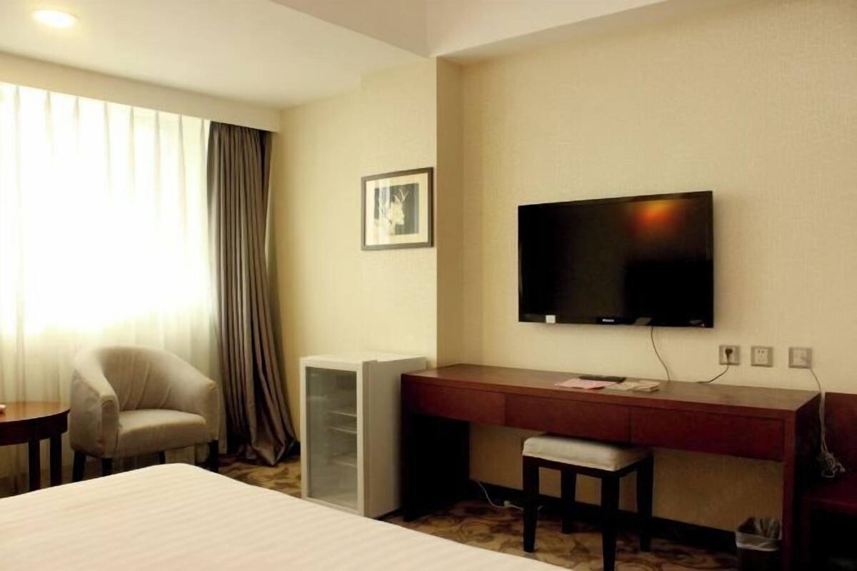 Une chambre d’hôtel comprenant un lit, un bureau avec une chaise, une télévision et une fenêtre avec des rideaux.
