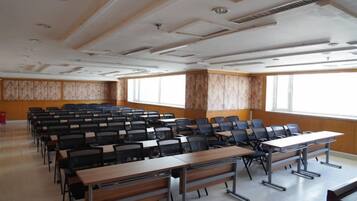 Un salón de conferencias con filas de sillas y mesas, ventanas amplias y un panel de pared de madera.
