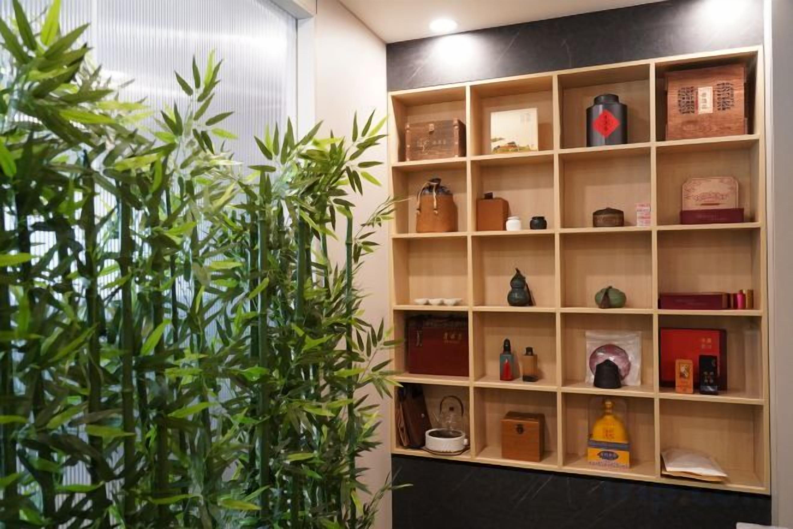 A room with a bamboo plant, wooden shelves, and various items including a clock, books, and decorative objects.