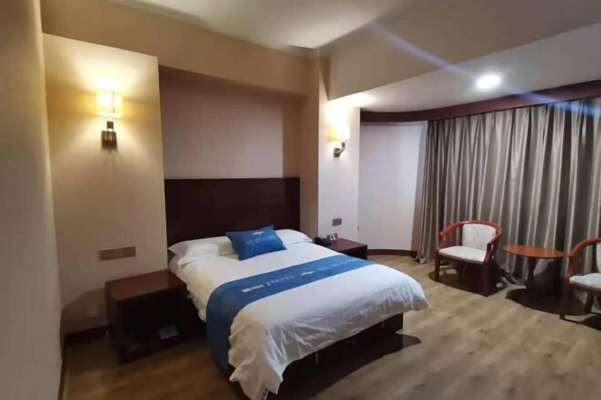 Une chambre d’hôtel avec un lit, des tables de chevet, une chaise, une petite table et un rideau.