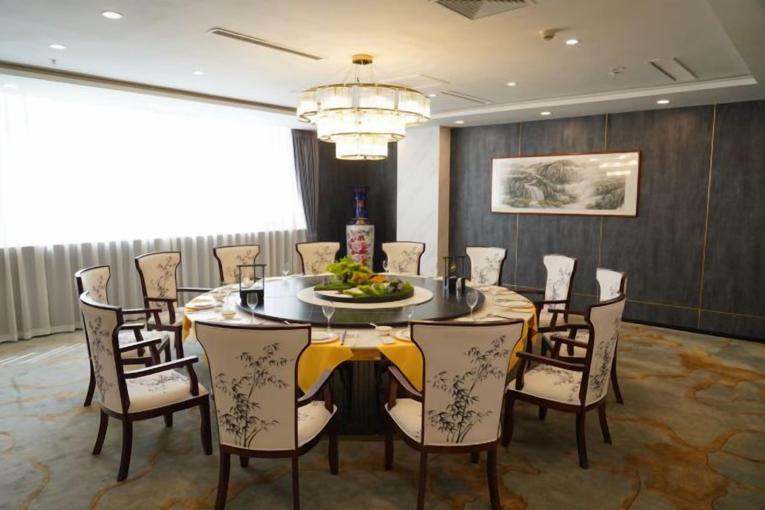 A conference room with a round table, chairs, a chandelier, and a painting on the wall.