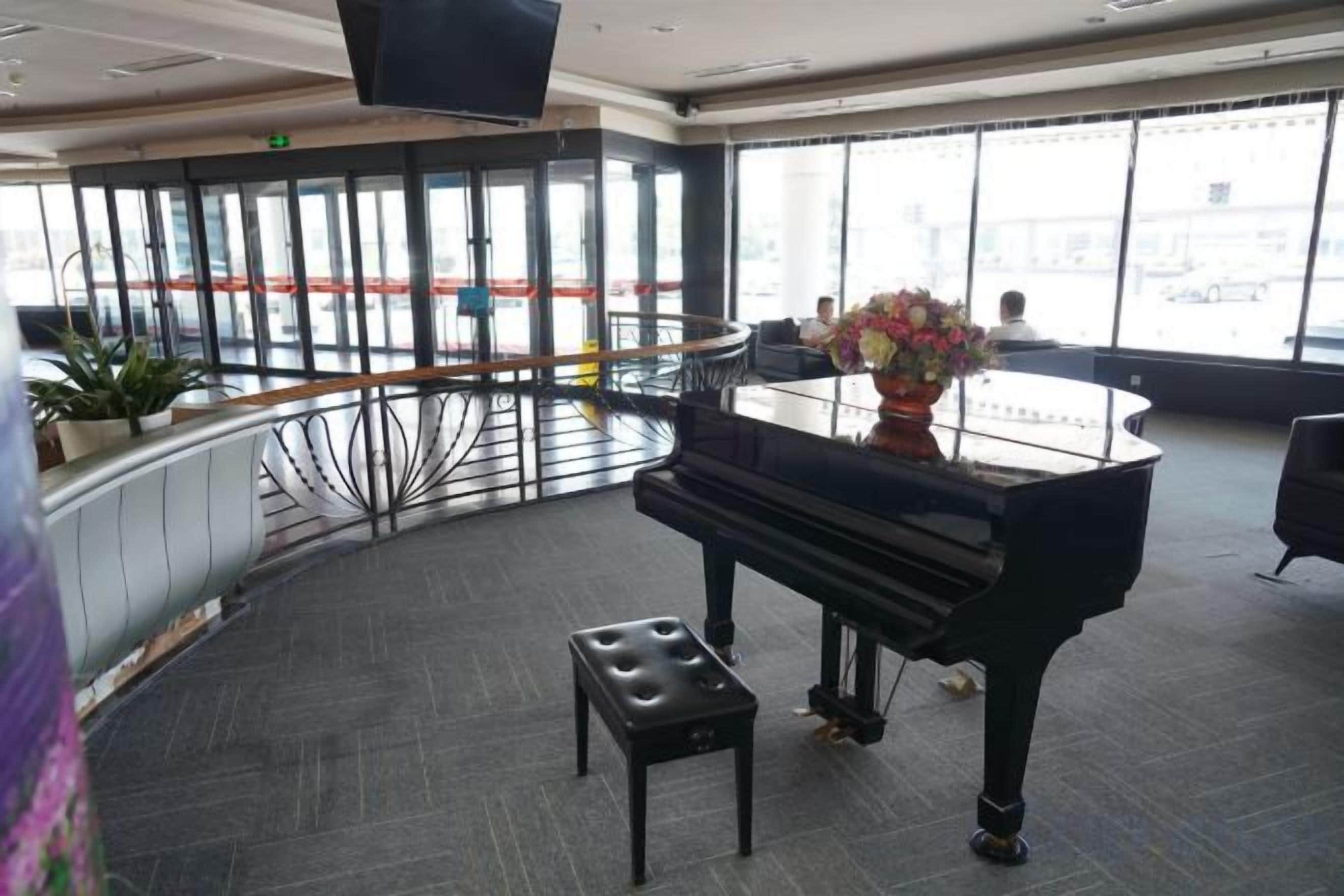Un piano de cola en una habitación amplia con una barandilla curva y un ventanal con vistas a la ciudad.