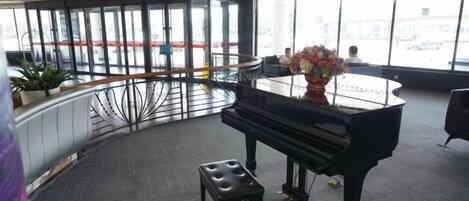 Un piano de cola en una habitación amplia con una barandilla curva y un ventanal con vistas a la ciudad.