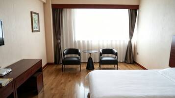 A hotel room with a bed, a desk, two chairs, a small table, and a window with curtains.