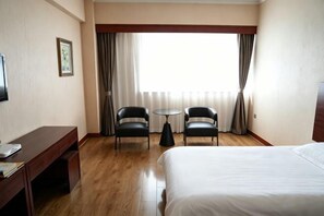 Habitación de hotel con cama, escritorio, dos sillas, una mesita y una ventana con cortinas.