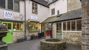 A courtyard with a stone well, a green door, and a building with a sign for 'ANI Skincare'. - Beautifully presented dog friendly - The Barley Apartment (Cirencester)