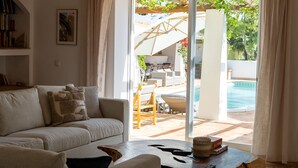 A living room with a sofa, a coffee table, and a view of an outdoor patio area with a pool. - Splendid Penina Country House Retreat (Portimão)