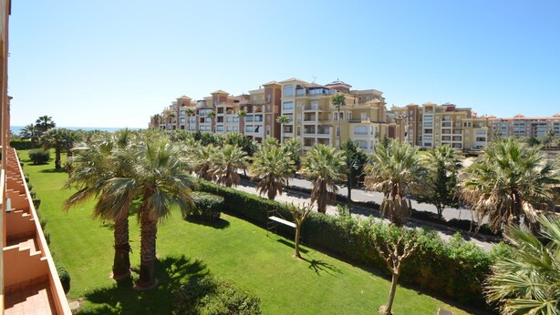 A multi-story hotel with a central courtyard surrounded by palm trees and a view of the sea. - Albatros 23 - Two Bedroom Apartment, Sleeps 5 (Punta del moral)