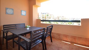 A balcony with a wooden table and chairs, two wall-mounted signs, and a view of buildings and palm trees. - Albatros 23 - Two Bedroom Apartment, Sleeps 5 (Punta del moral)