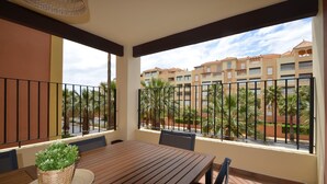A balcony with a wooden table and chairs, a potted plant, and a view of a residential building with palm trees. - Los Cisnes 13 - Two Bedroom Apartment, Sleeps 5 (Punta del moral)