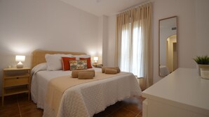 A bedroom with a bed, bedside tables, a mirror, and a potted plant. - Los Cisnes 13 - Two Bedroom Apartment, Sleeps 5 (Punta del moral)