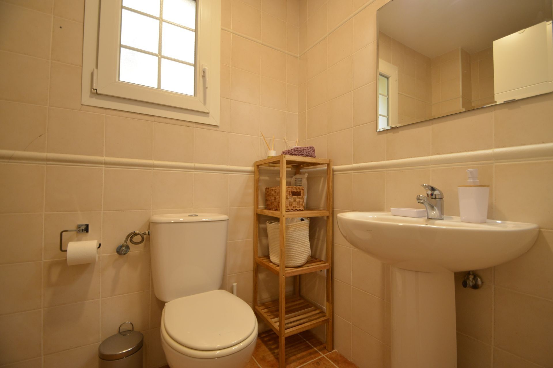 Ein Badezimmer mit Toilette, einem Holzregal mit Körben, einem Waschbecken und einem Spiegel.