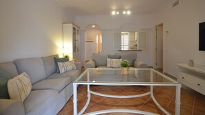 A living room with a glass coffee table, two sofas, a cabinet, and a TV on the wall. - Los Cisnes 13 - Two Bedroom Apartment, Sleeps 5 (Punta del moral)