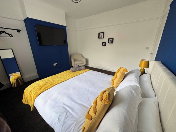 A hotel room with a bed, a chair, a TV, and a lamp.
