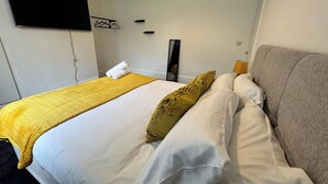 A hotel room with a bed, a TV mounted on the wall, a bedside table with a lamp, and a mirror. - City Centre-4 Br-sleeps 7-garden-free Parking (Newcastle-upon-Tyne)