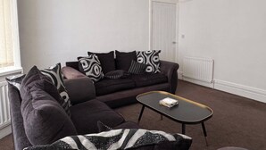 A living room with a dark-colored sofa, a matching armchair, and a small black coffee table with a book on it. - City Centre-4 Br-sleeps 7-garden-free Parking (Newcastle-upon-Tyne)