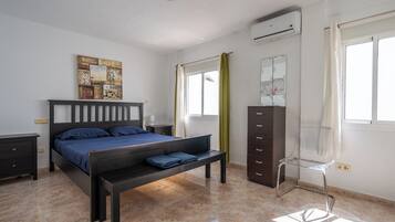Quarto com cama, um banquinho, cômoda e espelho.