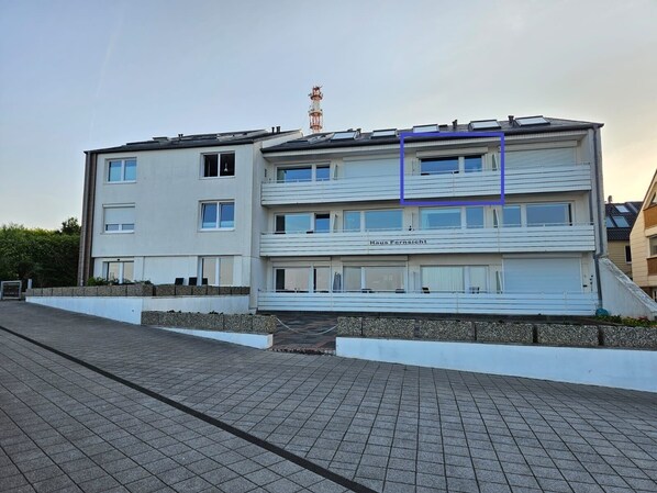 Un edificio residencial de varios pisos con techo plano, paneles solares y antena visible.
