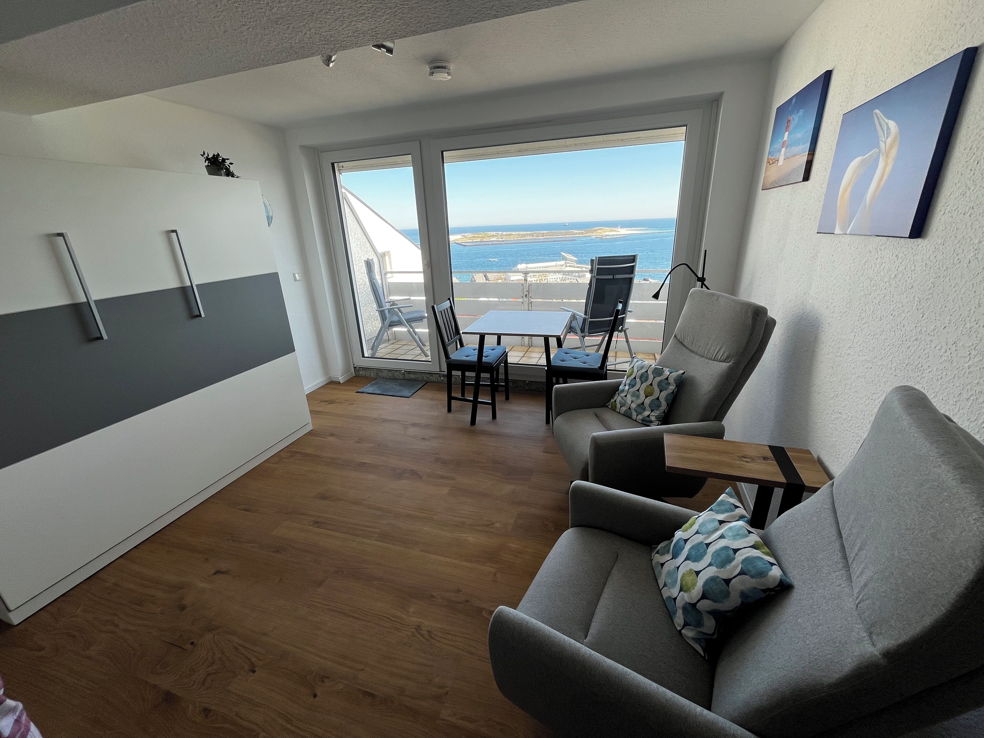A modern living room with a sofa, a small table, and a view of the sea through large windows.