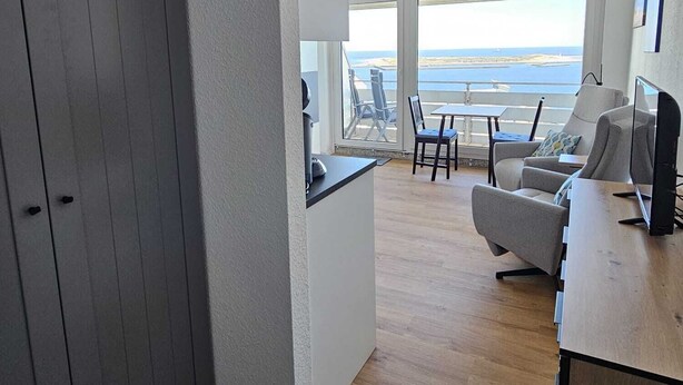 Een moderne woonkamer met uitzicht op zee, een eethoek en een grijze garderobe.