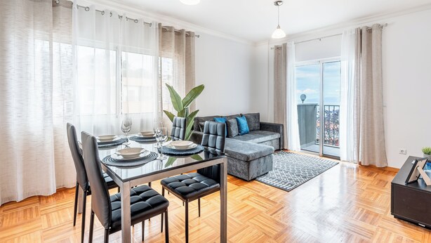 Ein modernes Wohnzimmer mit Essbereich, grauem Sofa und einem Balkon mit Aussicht.