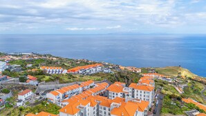 Ein Küstenwohngebiet mit orangefarbenen Dächern, freiem Blick auf das Meer und einer hügeligen Landschaft.