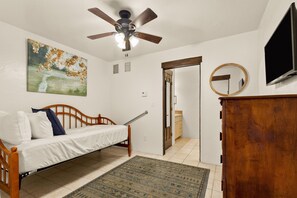A bedroom with a bed, a ceiling fan, a painting, a television, and a wooden cabinet.