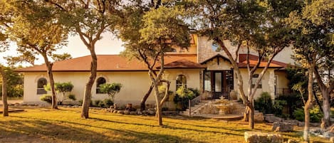 A house with a stone facade, a red roof, and a front yard with trees and a stone fountain.