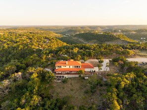 A large house with a red roof surrounded by dense forest and hills.