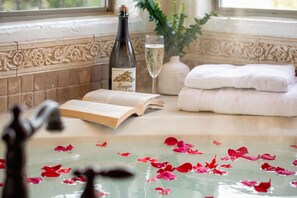 A bathtub with rose petals, a bottle of wine, a glass of champagne, and a book.